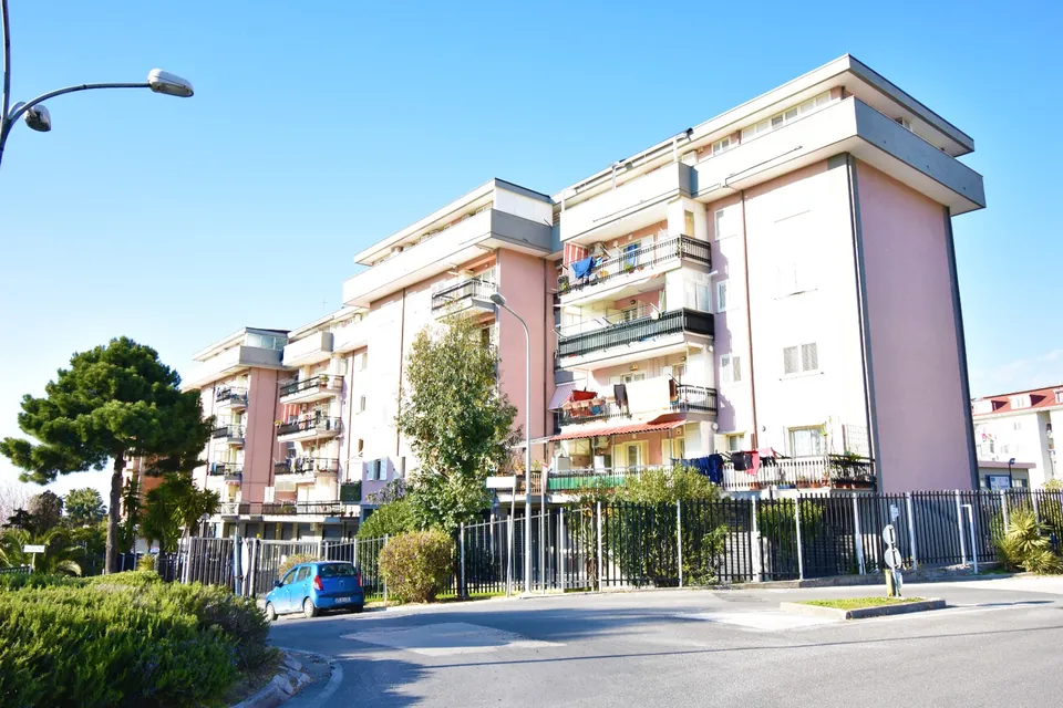 Una palazzina residenziale rosa di cinque piani con i balconi affacciati sulla strada, vista da fuori la cancellata
