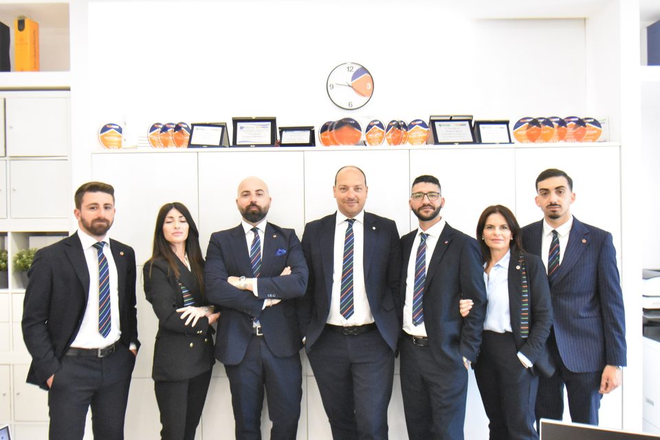 I sette componenti del team dell'agenzia davanti alla parete dei riconoscimenti